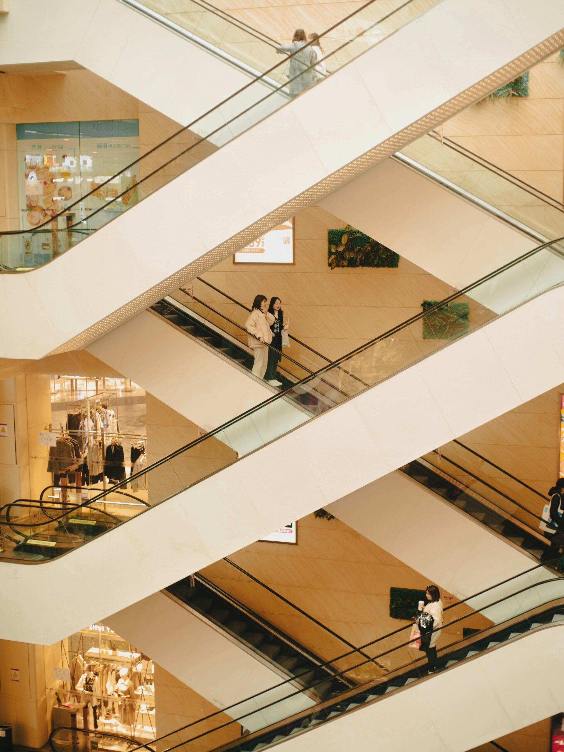 People riding escalators in a modern shopping mall with glass storefronts and stylish architecture.